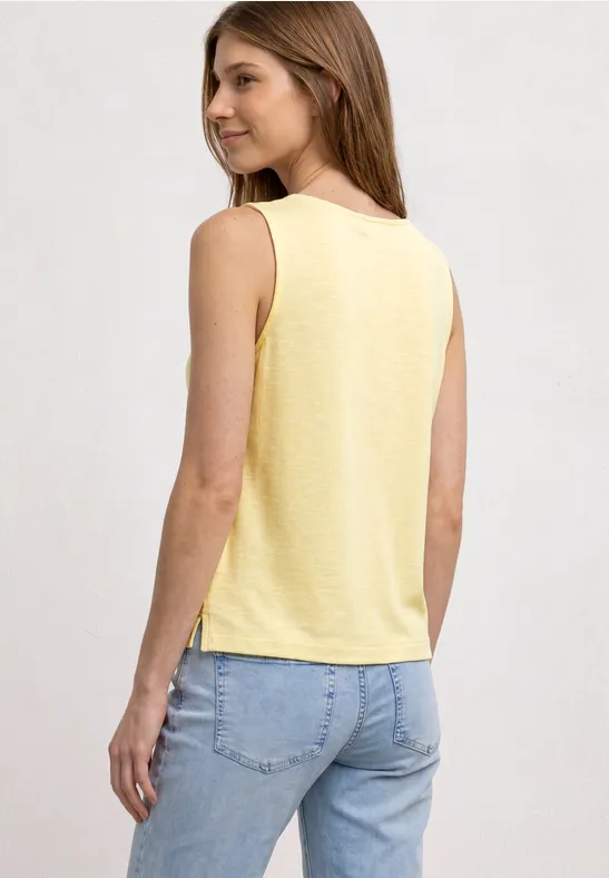 Eine Frau von hinten in einem gelben ärmellosen Top und hellblauen Jeans.