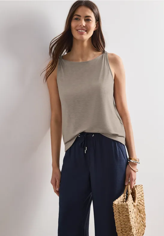 Frau in grauem Top und dunkelblauer Hose hält eine geflochtene Strohtasche.