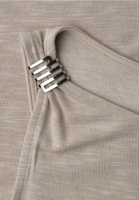 Nahaufnahme eines beigen Stricktops mit silbernen Rechteck-Clips am Träger und feiner Rippstruktur.