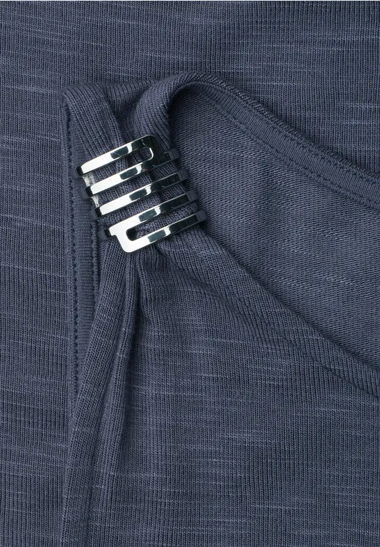 Nahaufnahme eines dunkelblauen Strickstoffs mit drei silbernen Metallhaken, die zwei Stofflagen verbinden.