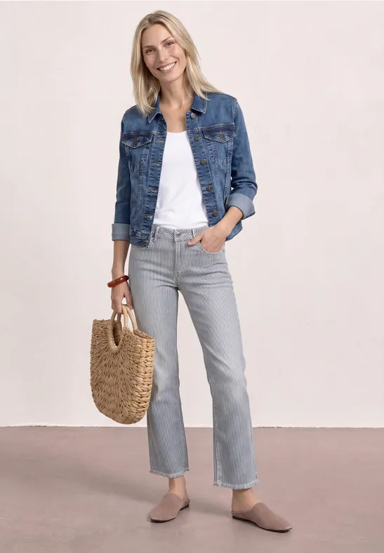 Frau in Jeansjacke, weißem Top, grauen Jeans, beigen Slippern und geflochtener Tasche.
