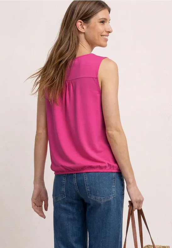 Femme de dos en top rose sans manches, jean et sac marron devant un fond clair.