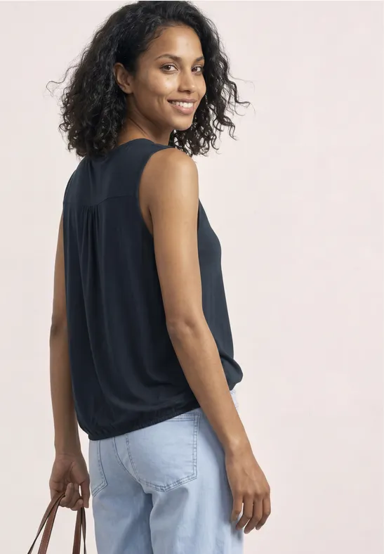 Vrouw in een zwart mouwloos topje en lichtblauwe jeans, met een handtas in de hand.