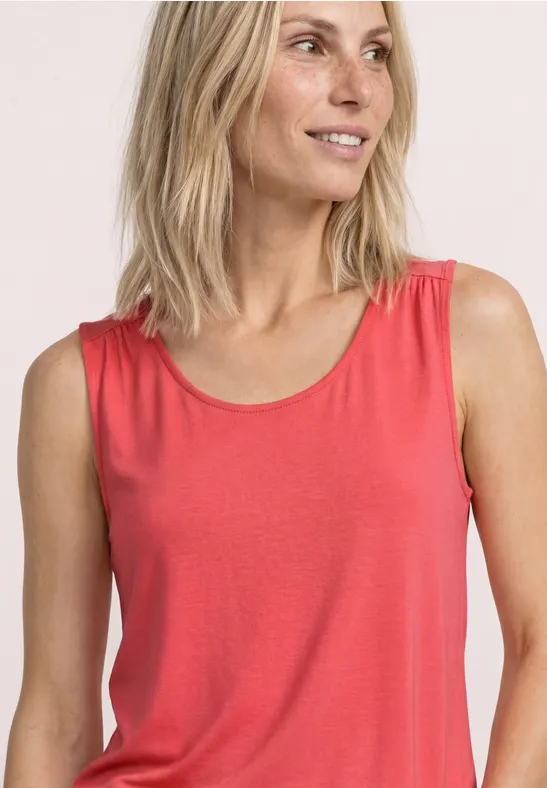 Frau mit blonden Haaren trägt rotes ärmelloses Top.