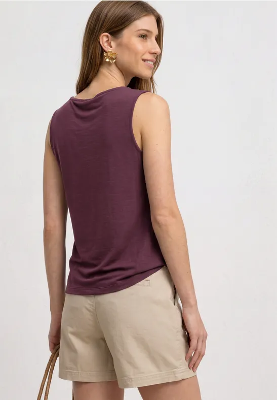 Frau von hinten in lila Top und beigen Shorts, hält eine Tasche in der Hand.