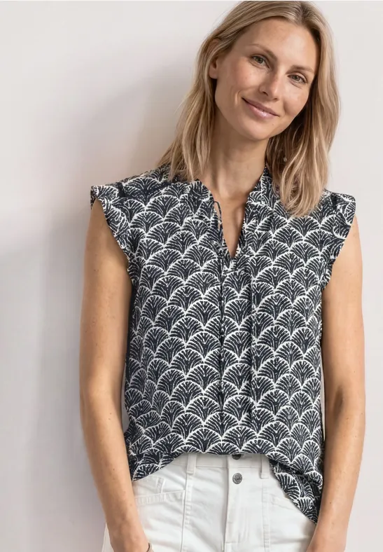 Vrouw in mouwloze blouse met zwart-wit geometrisch patroon, aan de voorkant ingetrokken.