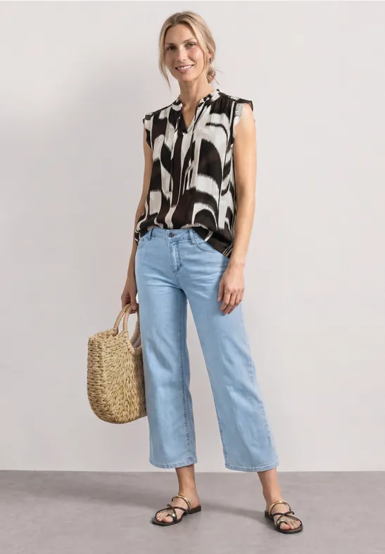 Femme en blouse sans manches noir et blanc, jean raccourci bleu clair, sandales noires et panier en osier.