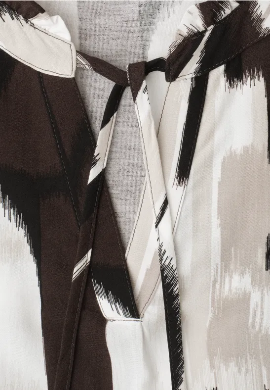Gros plan sur un vêtement à motif abstrait coups de pinceau noir, beige et blanc, avec nœud près de l'encolure