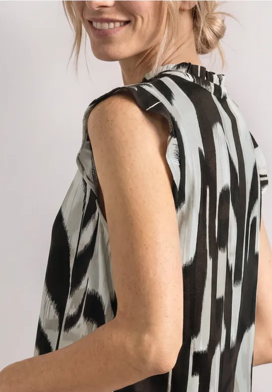Femme en chemisier sans manches à motif noir et blanc, vue de côté, cheveux relevés en chignon.