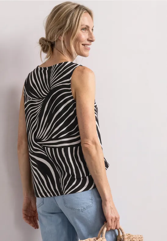 Kobieta od tyłu w topie w zebrę, blond kok, dżinsy i słomiana torba