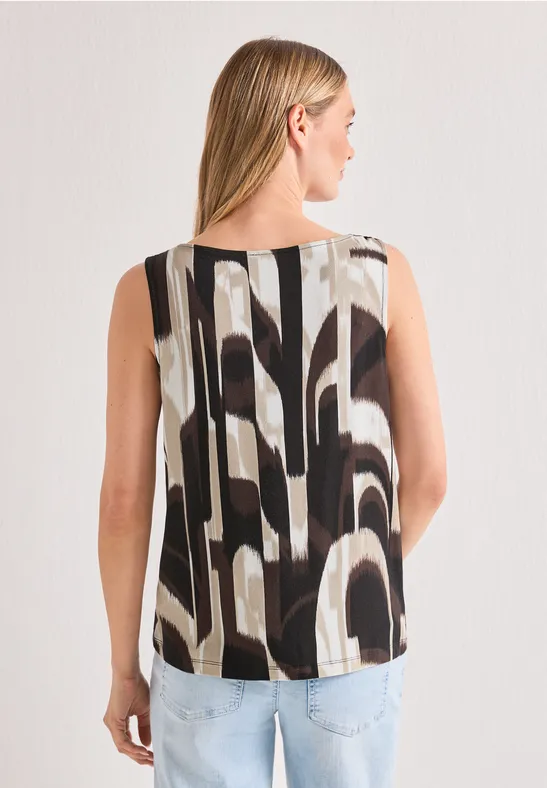 Femme de dos portant un top sans manches à motif abstrait noir et blanc et un jean bleu clair.