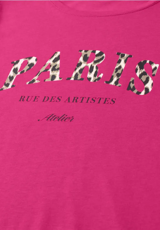 Ein pinkes Shirt mit gemustertem Schriftzug 'PARIS Rue des Artistes Atelier'.