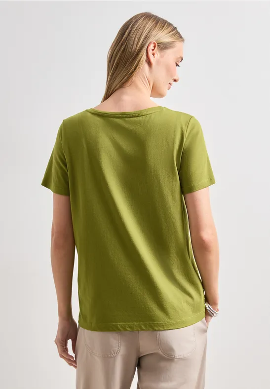 Rückansicht einer Frau in grünem T-Shirt und beiger Hose.