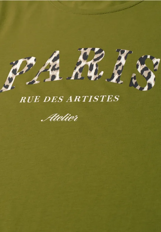 Ein olivgrünes T-Shirt mit dem Schriftzug 'PARIS' in Camouflage-Muster, darunter 'RUE DES ARTISTES' und 'Atelier' in Weiß.