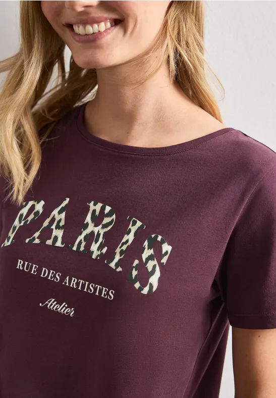 Frau trägt Burgunderfarbenes T-Shirt mit Blumen-Print 'PARIS' und Schriftzug 'Rue des Artistes'.