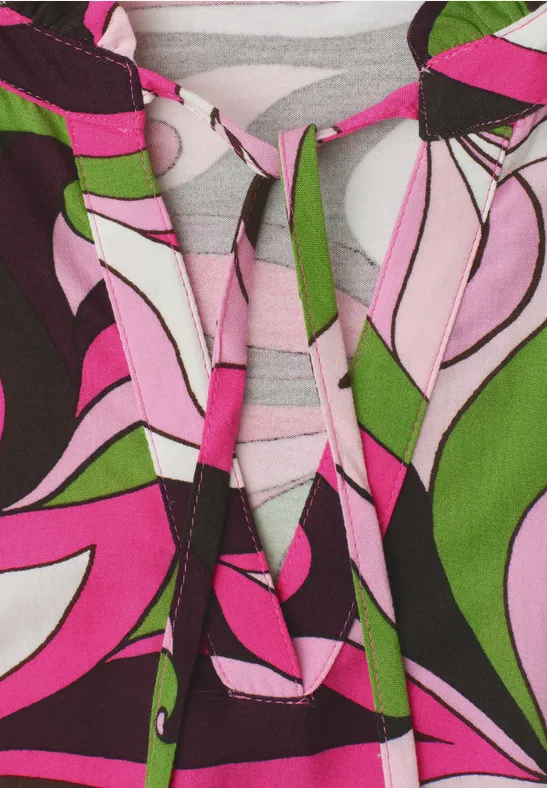 Nahaufnahme eines bunten Kleids mit pink-grünen und schwarzen Mustern und Schnürdetail am Ausschnitt.