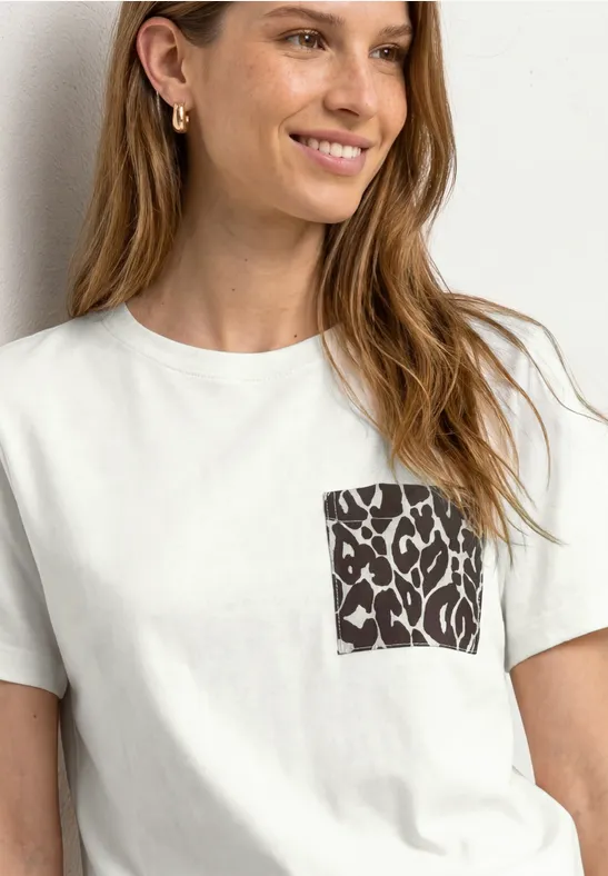Frau trägt weißes T-Shirt mit schwarzem Leo-Muster auf der Brusttasche.