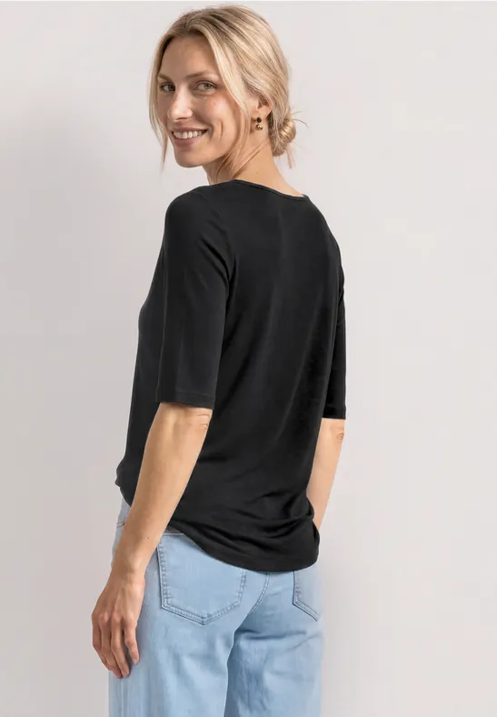 Vrouw van achteren in een zwart T-shirt met halflange mouwen en een lichte spijkerbroek voor een neutrale achtergrond.