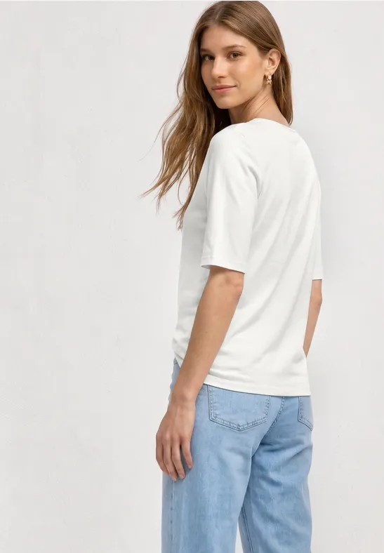 Vrouw van achteren in een wit t-shirt en blauwe spijkerbroek tegen lichte achtergrond.