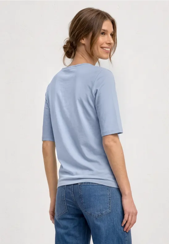 Vrouw van achteren in lichtblauw T-shirt en spijkerbroek.