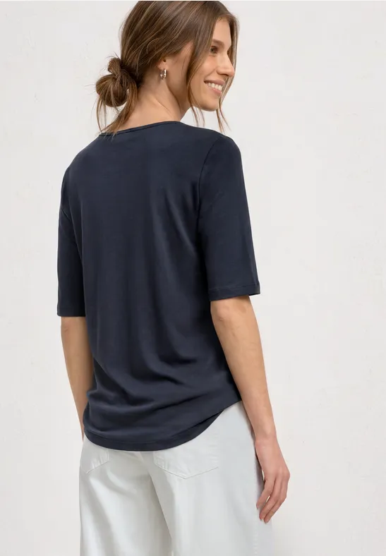 Vrouw van achteren in een los vallend donkerblauw t-shirt met halve mouwen en lichte broek.
