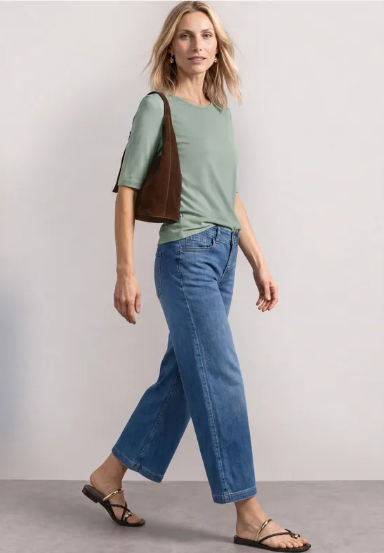 Vrouw in groen shirt, jeans en sandalen met bruine schoudertas, zijaanzicht