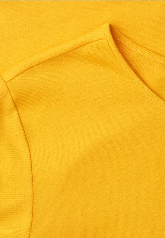 Close-up van een geel T-shirt met zichtbare naad bij mouw en hals.