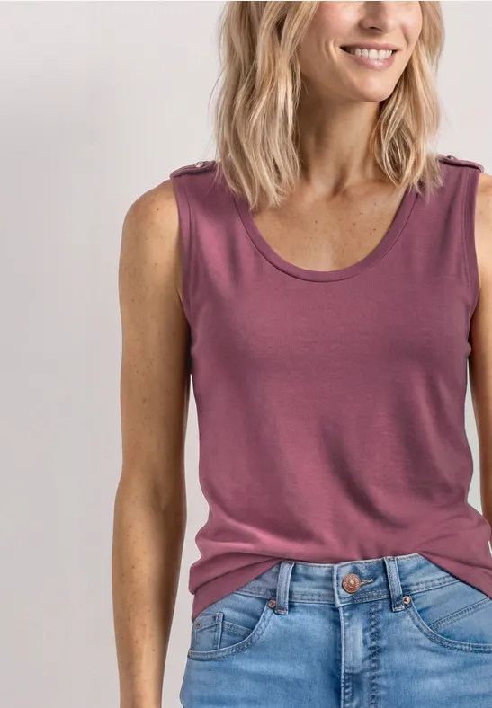Frau trägt ärmelloses, rosafarbenes Top und blaue Jeans vor weißem Hintergrund.