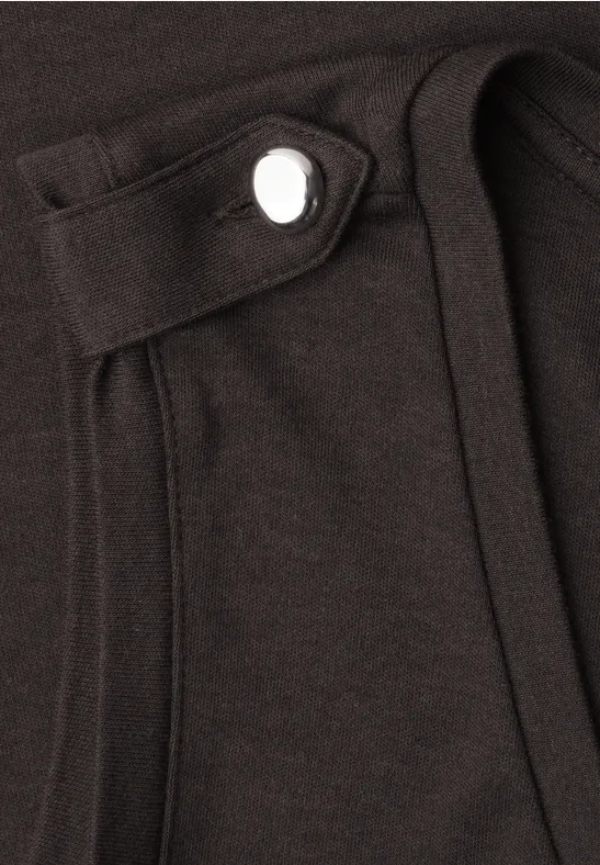 Nahaufnahme eines schwarzen Kleidungsstücks mit aufgesetzter Tasche und sichtbarem Druckknopf