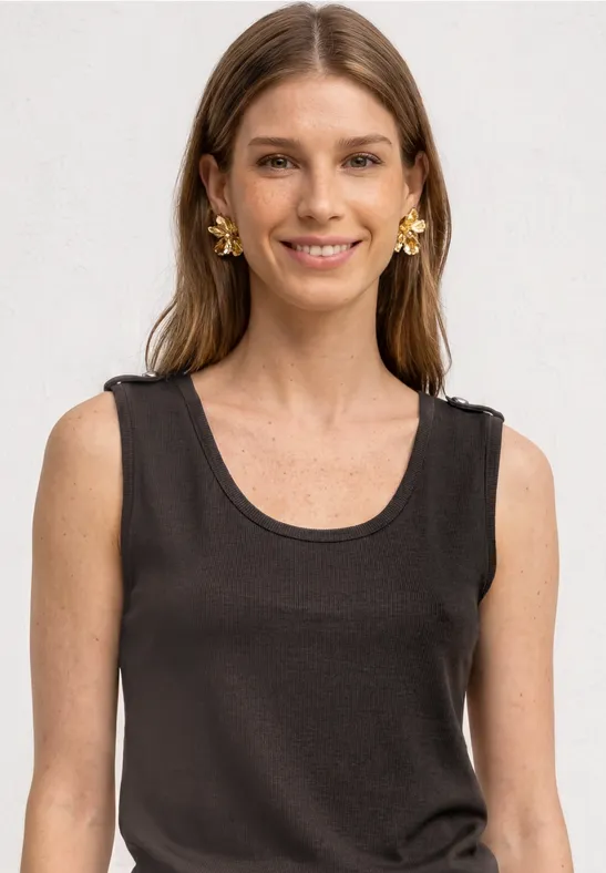 Frau in einem ärmellosen schwarzen Top, lange Haare und goldene Ohrringe vor weißem Hintergrund.