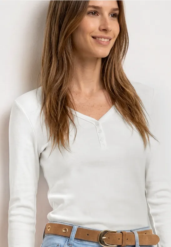 Lachende vrouw in een wit langärmelig V-hals shirt met lichtbruine riem.