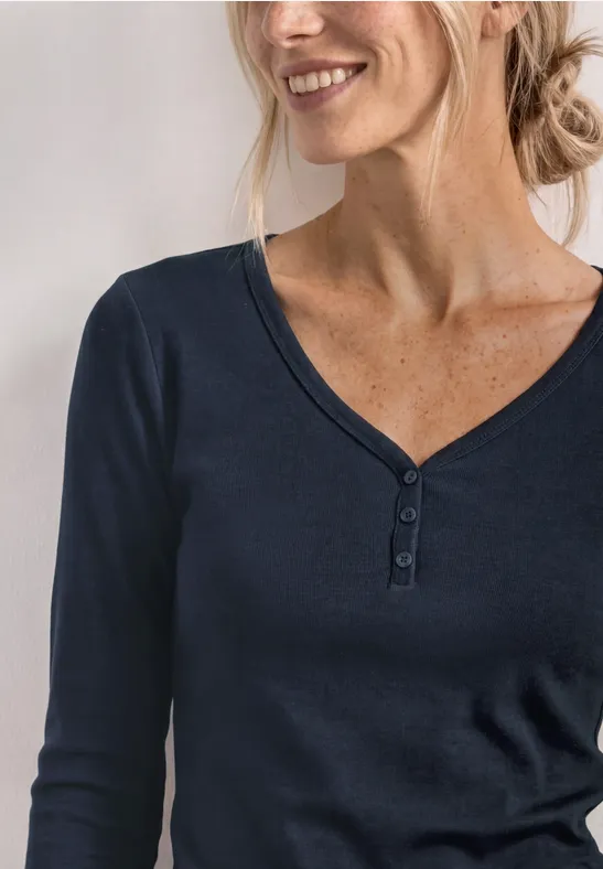 Een lachende vrouw draagt een navyblauw shirt met lange mouwen, V-hals en knoopsluiting.
