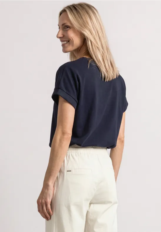 Vue latérale d'une femme portant un t-shirt bleu marine et un pantalon clair sur fond blanc
