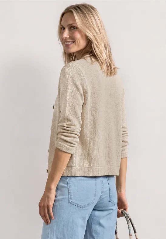 Frau von hinten in beigem Strickjäckchen und blauen Jeans, die eine Handtasche hält.