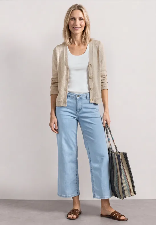 Frau trägt hellblaue Jeans, weißes Top, beigen Cardigan, braune Sandalen und gestreifte Tasche.