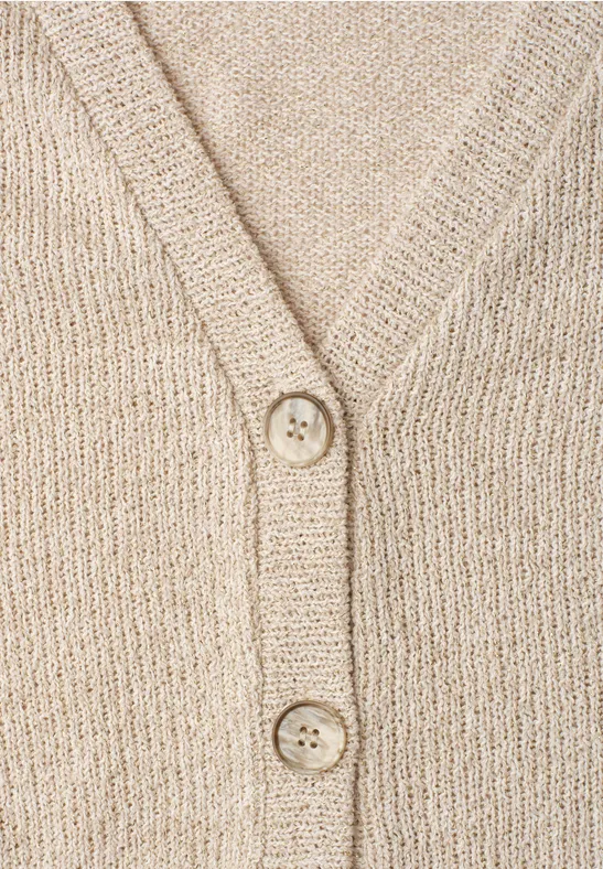 Nahaufnahme eines beigen, grob gestrickten Cardigans mit V-Ausschnitt und zwei Knöpfen.