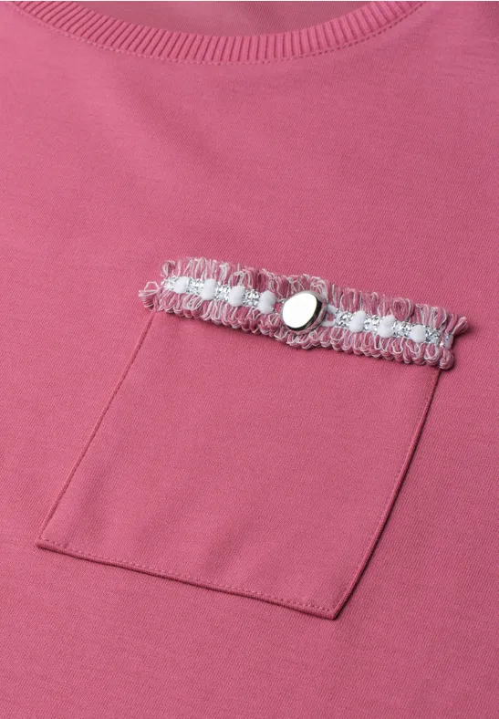Pinkes Shirt mit quadratischer Brusttasche, verziert mit grauer Spitzenborte und silbernem Knopf.