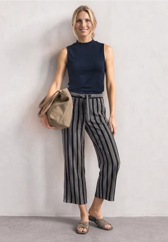 Frau trägt marineblaues Top, gestreifte Culotte-Hose, Sandalen und hält eine beige Tasche.