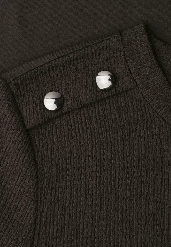 Nahaufnahme eines schwarz strukturierten Kleidungsstücks mit zwei silbernen Druckknöpfen.