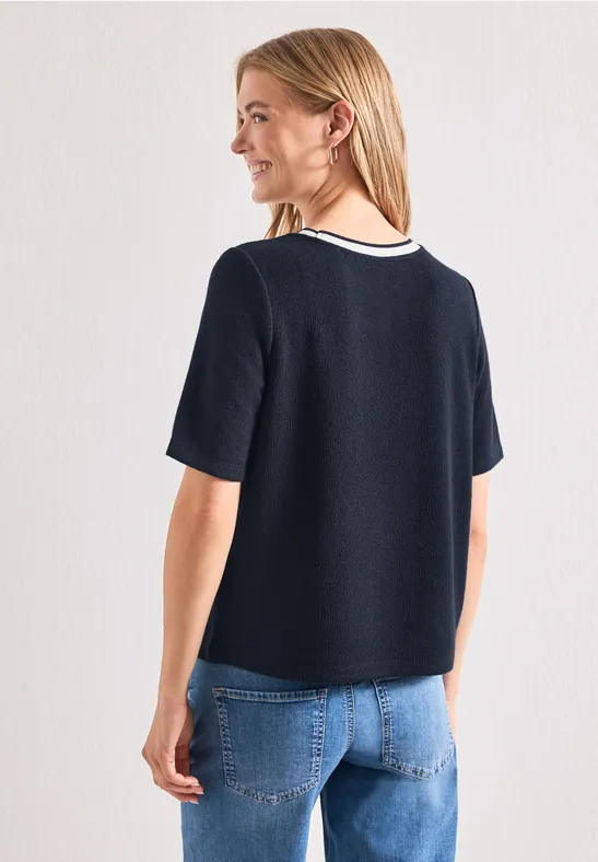 Vrouw van achteren in een donkerblauw T-shirt met witte kraag en een blauwe spijkerbroek.