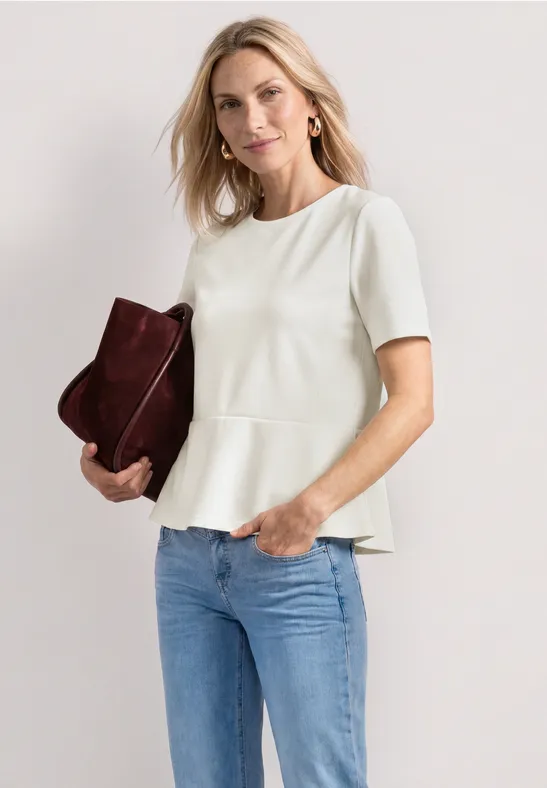 Vrouw in wit peplumshirt met korte mouwen en spijkerbroek, houdt een bordeaux clutch vast.