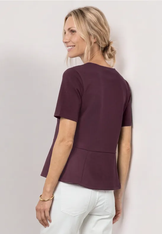 Frau von hinten in dunkelrotem Top und weißer Hose, blondes Haar locker hochgesteckt