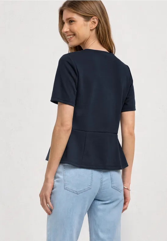 Vrouw van achteren met donkerblauw T-shirt met korte mouwen en lichtblauwe jeans, kijkt om en lacht.