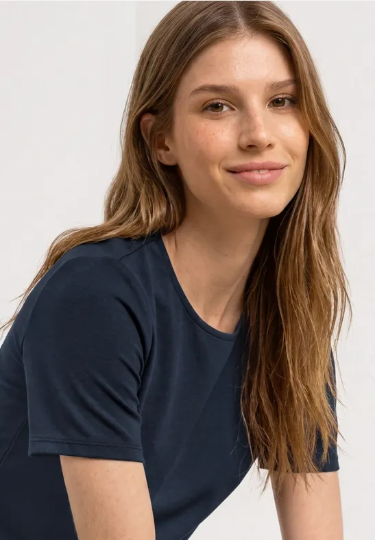 Een persoon met lang blond haar draagt een donkerblauw T-shirt voor een lichte achtergrond.