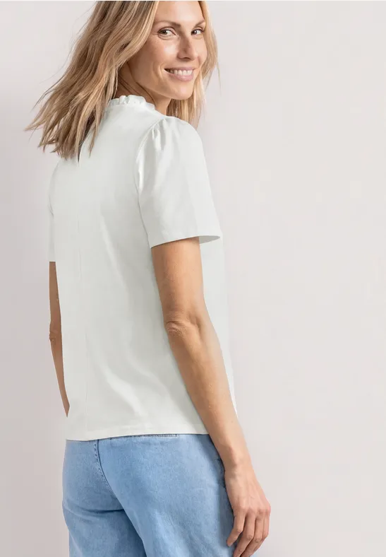 Een vrouw van achteren draagt een wit T-shirt en blauwe spijkerbroek tegen een neutrale achtergrond.