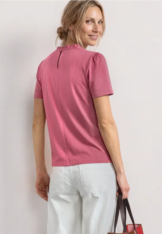 Frau von hinten in pinkem T-Shirt, weißen Jeans und Handtasche in der Hand.
