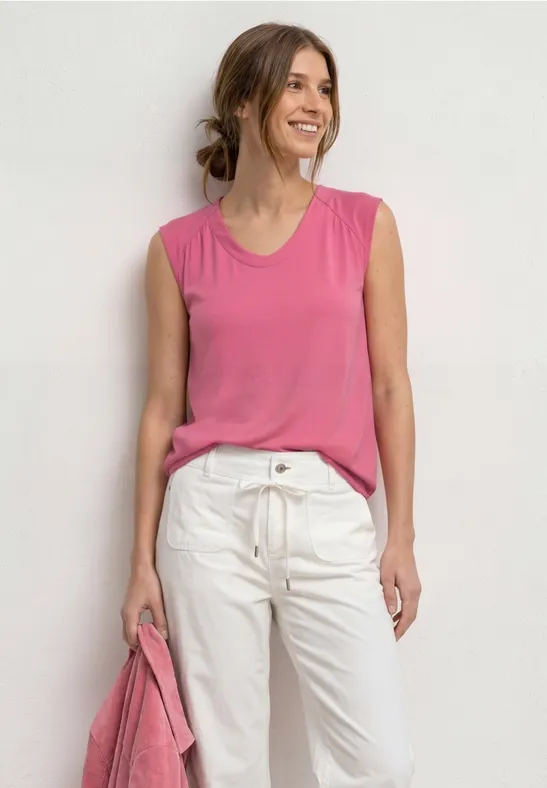 Vrouw draagt roze mouwloze top en witte broek, houdt een roze tas vast.