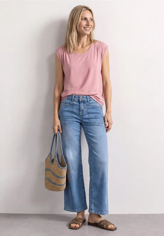 Vrouw in roze top, blauwe wijde jeans en sandalen met een strandtas.