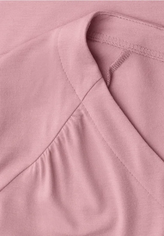 Close-up van een roze shirt met fijne stiknaden bij de halslijn.