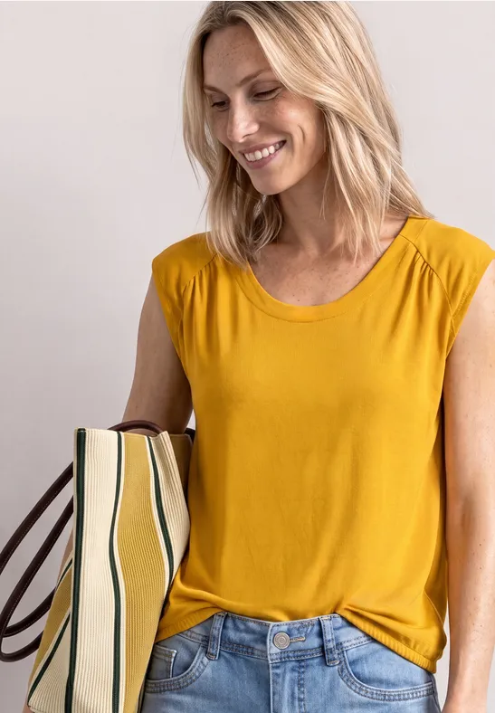 Une femme blonde souriante en t-shirt jaune et jean, tenant un sac rayé.